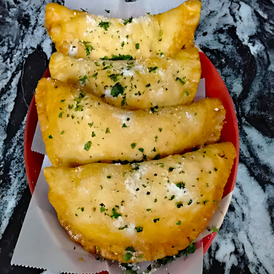 Four golden-brown fried calzones, topped with parsley and parmesan, on a red plate.